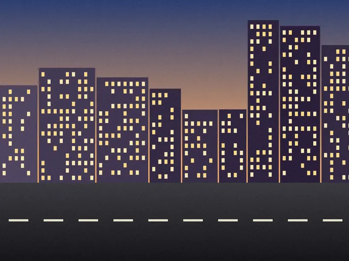 An invented city street at dusk, with lit windows in the buildings.